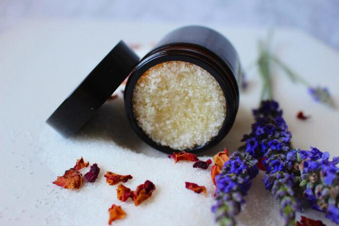 a jar of sugar scrub next to purple flowers.