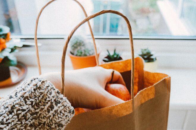 A hand grabbing an apple from a brown shopping bag.