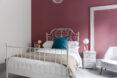 A bedroom with a white bedspread and medium toned mauve walls.
