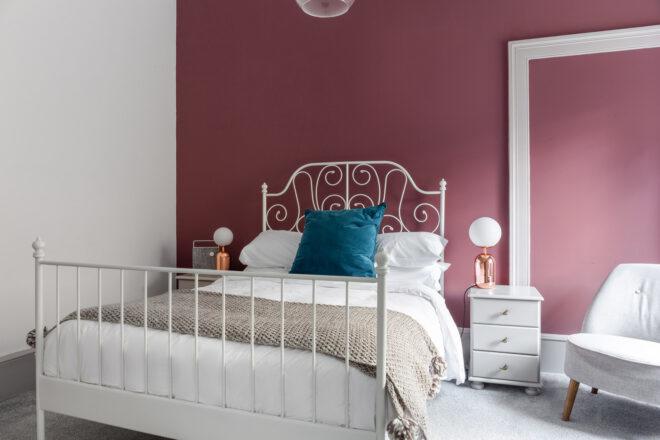 A bedroom with a white bedspread and medium toned mauve walls.