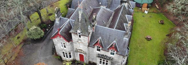 An aerial photo of a 19th century building with grey stone and red accents.
