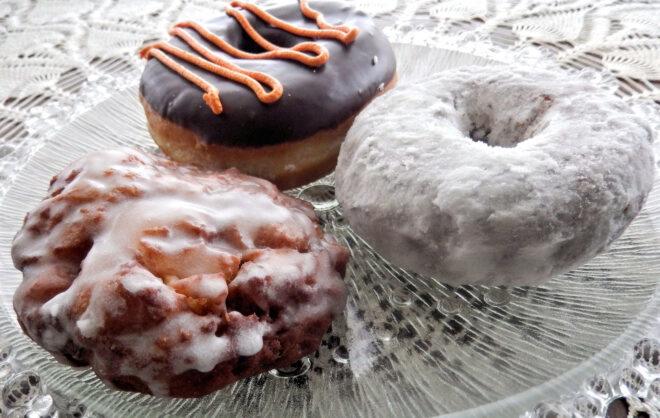 apple fritter, powdered donut and chocolate donut on glass platter