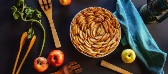 apple pie on black background with wood spoons and apples