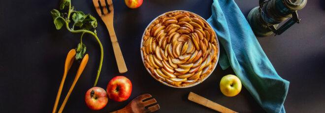 apple pie on black background with wood spoons and apples