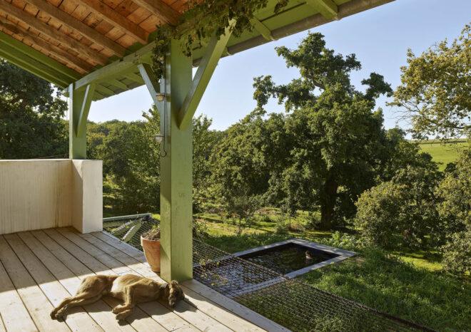 A covered terrace with next to a green lawn, with a dog laying on the porch.