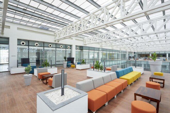An indoor sitting area with orange, white, yellow and blue sofas. White industrial bars are overhead.
