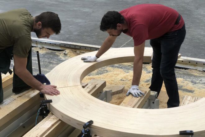 Two people putting together pieces of the wood Circula bench.
