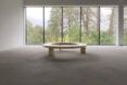 A wood Circula bench in an empty room in front of windows.