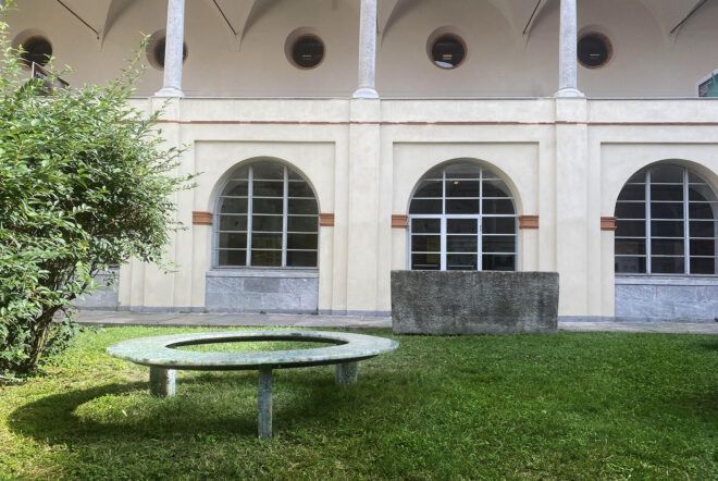 A plastic Circula bench outside in the grass, with a building in the background.