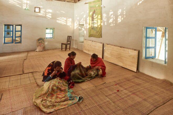 people weaving textiles in large, open room