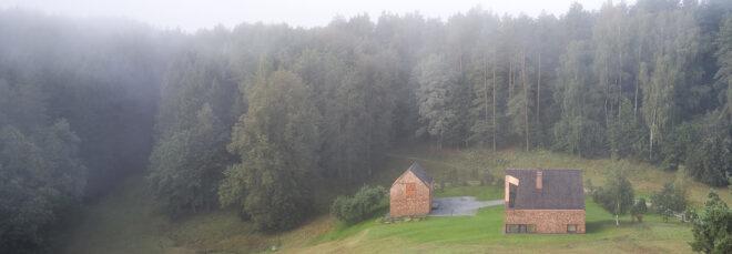 foggy hillside with a wood gabled home and smaller wood gabled building next to the home