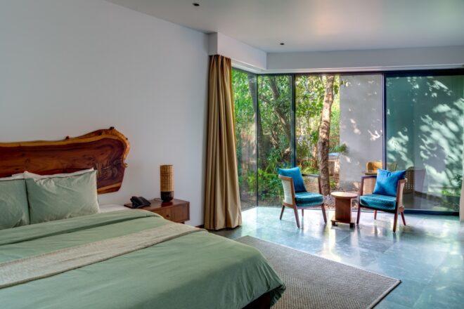 mint-colored bed in white room with blue chairs near walls of glass