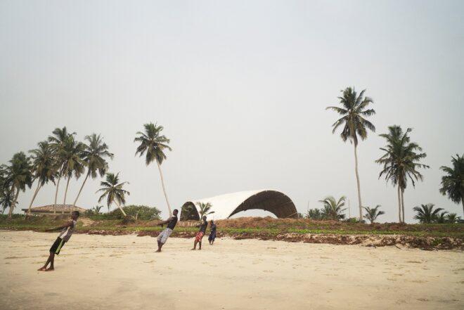 people pulling rope on beach near large bamboo arch