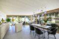 rendering of long dining table and light wood kitchen in apartment with walls of glass