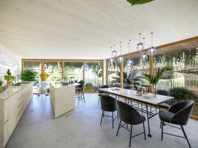 rendering of long dining table and light wood kitchen in apartment with walls of glass