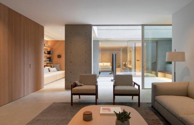 wood coffee table and beige chairs in room with glass walls connecting to a courtyard