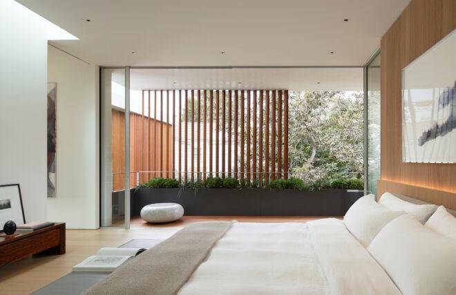 large white bed in room with wall of glass behind wood screen