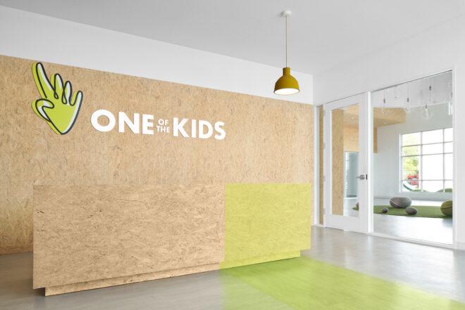 unfinished wood wall with sign that reads, "One of the Kids"