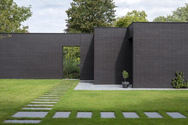 The back of the home, showing detail on the black brick facade. A stepstone path leads to a gated door within the wall.