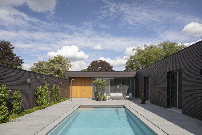 A swimming pool surrounded by the black brick home on three sides.