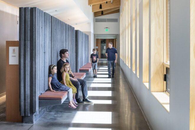 people sitting on benches looking out windows in a hallway