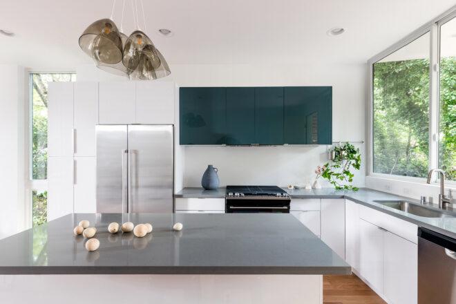 A kitchen with a gray island with built-in sink. In the background, there countertops, a stove, a frdige and an additional sink.