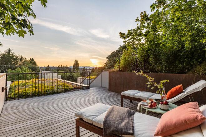 A patio area with two white lounge chairs and a small coffee table with apples and wine. Greenery surrounds the patio area.