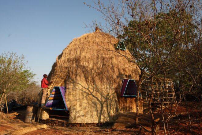 A person working on a thatched dome building.
