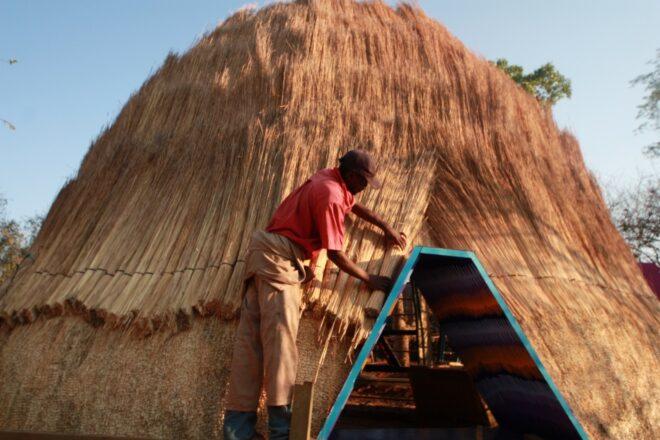 A person working on a thatched dome building.