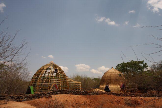 To the left, the skeleton of a dome being constructed. To the right, a complete thatched dome building.