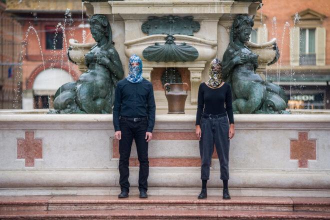 two people wearing sequin masks standing by a fountain