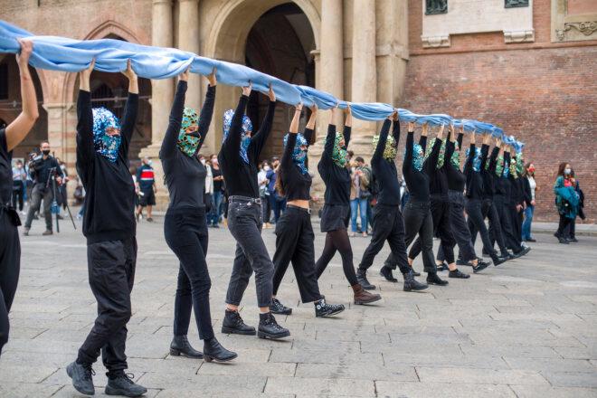 line of people dressed in all black and holding a blue cloth