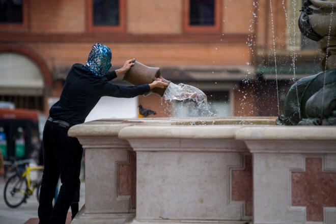person dumping vessel of water in a fountain