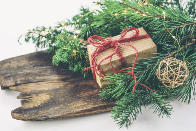 Greenery and a brown paper packaged tied up with red string sit atop a wood board.