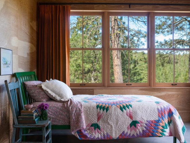 bed with quilt in room with large windows