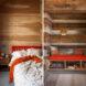 On the left, orange and white bed near windows. On the right, orange bench built into wall.