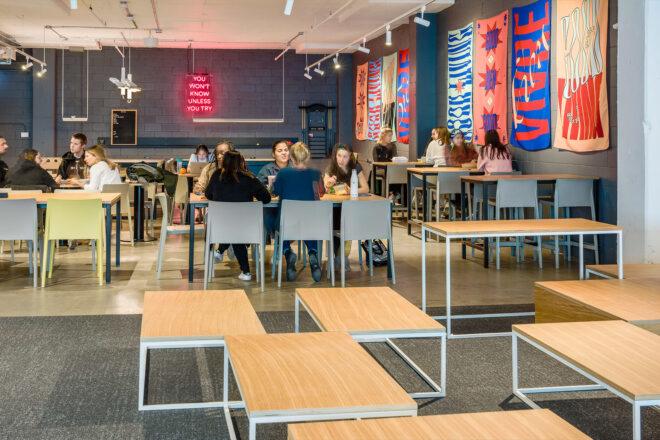 people dining in gray cafe room with colorful flags on the wall