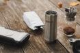 metal travel mug, powerbank and bag of coffee on picnic table