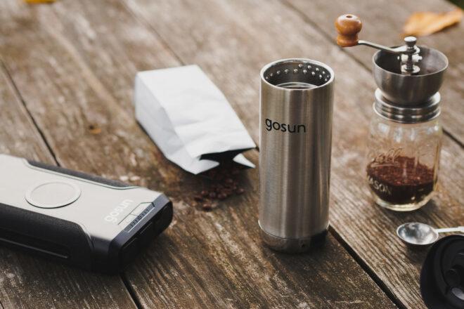 metal travel mug, powerbank and bag of coffee on picnic table