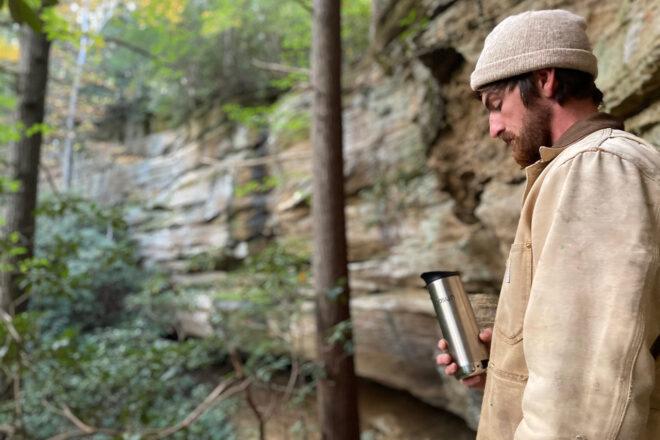 person holding metal travel mug while hiking
