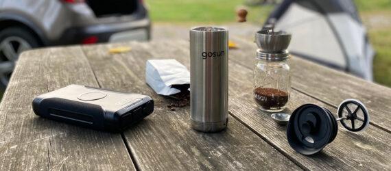 metal travel mug, powerbank and bag of coffee on picnic table