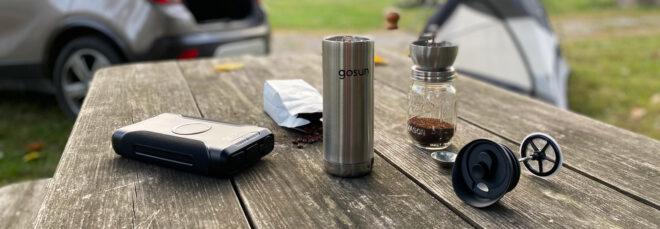 metal travel mug, powerbank and bag of coffee on picnic table