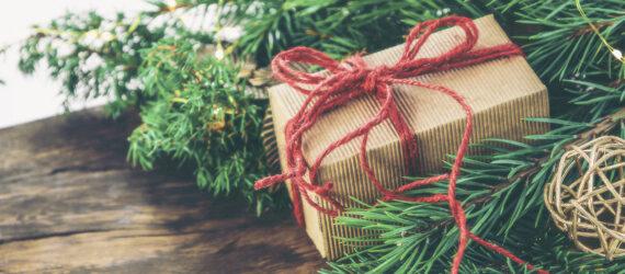 Greenery and a brown paper packaged tied up with red string sit atop a wood board.