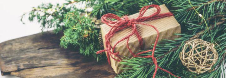 Greenery and a brown paper packaged tied up with red string sit atop a wood board.