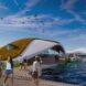 A rendering of the campus with curved-roof buildings near water. People mill around the area.