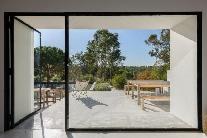 A floor-to-ceiling glass door and wall look out onto a patio with a table and chairs.