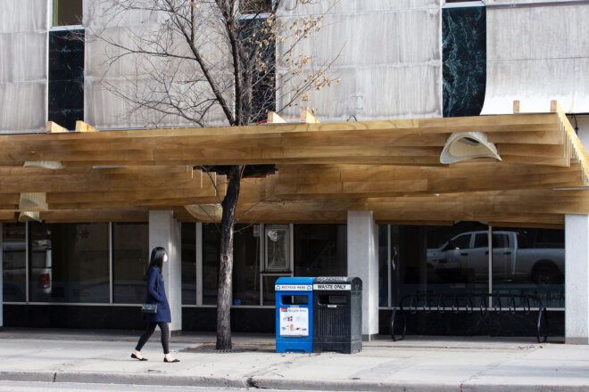 A daytime shot of a person passing under a wood canopy.