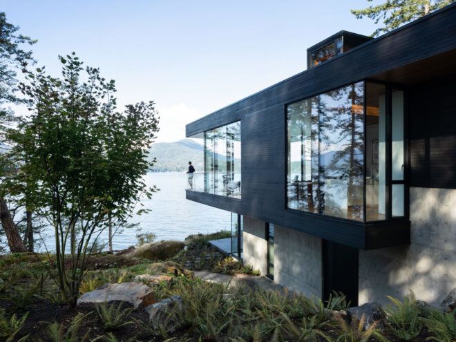 charred cedar and glass cabin on hill facing water