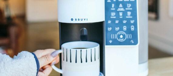 person grabbing mug of hot coffee from under a white coffee machine