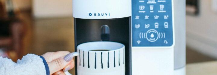 person grabbing mug of hot coffee from under a white coffee machine